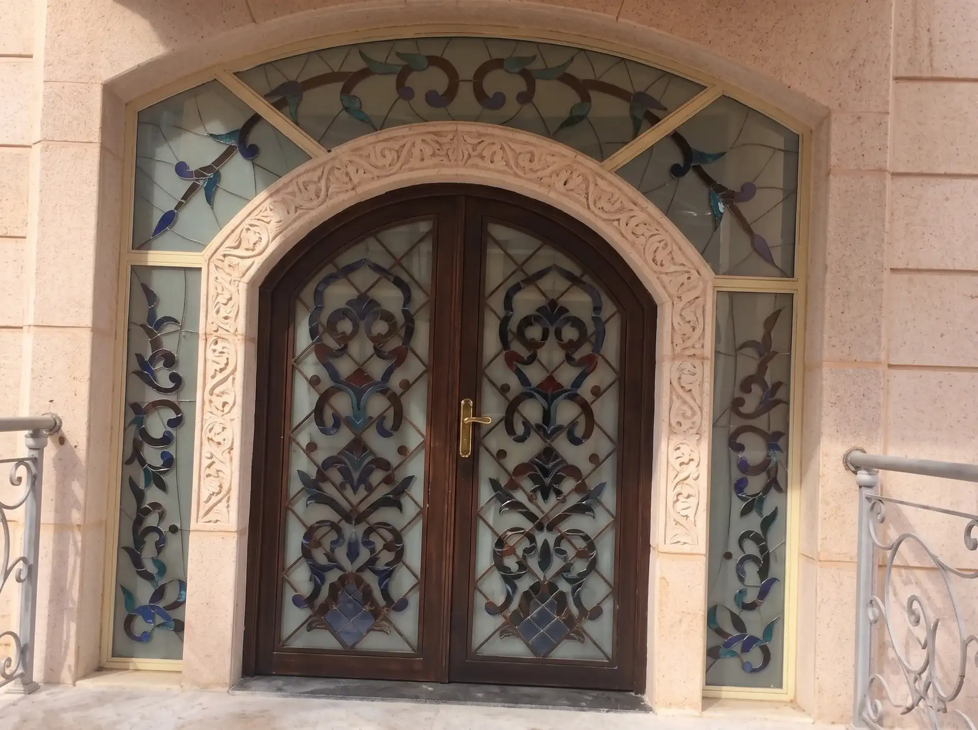 مدخل مقوس بباب مزدوج وزجاج معشق بزخارف زرقاء في واجهة حجرية